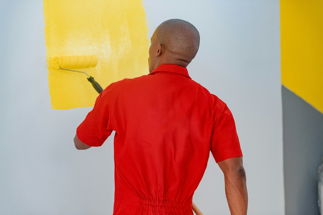 Cómo Reparar Grietas y Agujeros en Paredes de Yeso y Pintura con Masilla: a man painting a wall with yellow paint