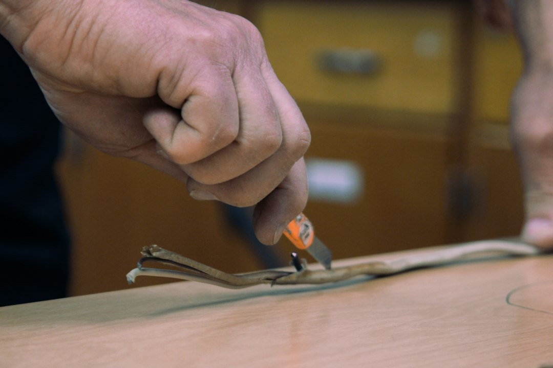 Cómo Renovar Muebles de Cocina Pintando las Puertas con Esmalte Sintético: a man is cutting a piece of wood with a pair of scissors