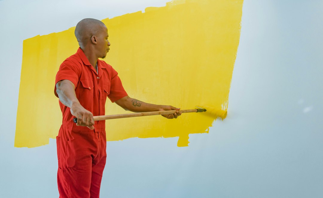 Guía para Instalar un Tabique de Pladur con Aislamiento Acústico: a man painting a wall with yellow paint