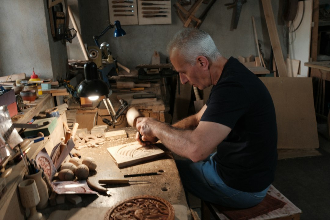 Técnicas de Envejecido y Efecto Pátina en Muebles de Madera Maciza: An elderly man meticulously carves wood in his workshop
